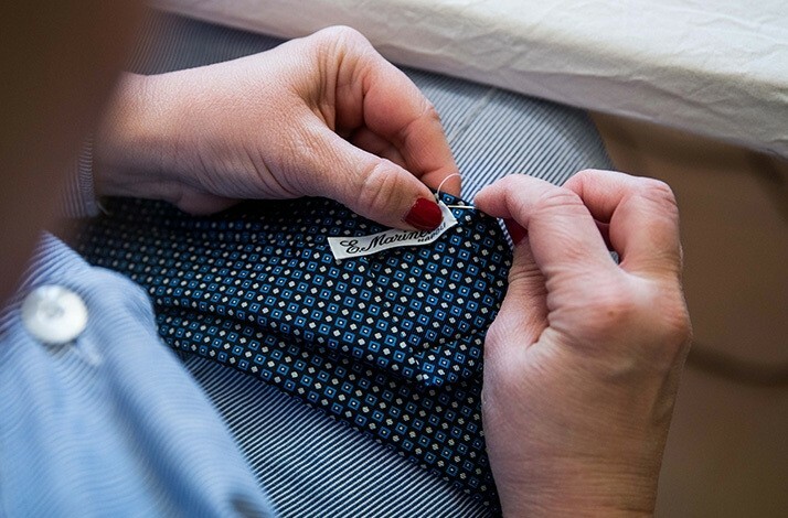 A seamless manual sewing of Eugenio Marinella brand label to a tie.