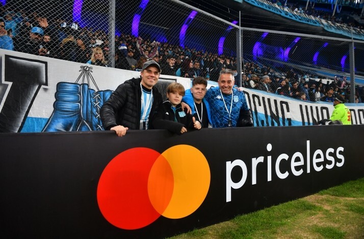 People in blue and white football jerseys posing next to a banner with Mastercard and priceless logos