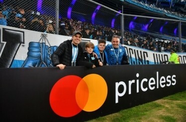 People in blue and white football jerseys posing next to a banner with Mastercard and priceless logos