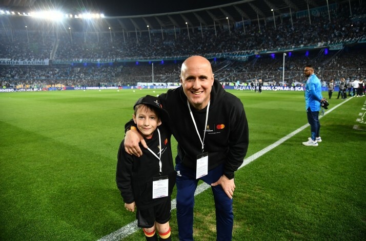 An adult and a child in sweatshirts with Mastercard logo posing on a football field