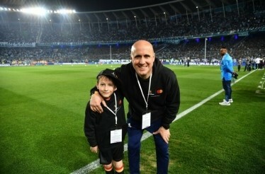 An adult and a child in sweatshirts with Mastercard logo posing on a football field