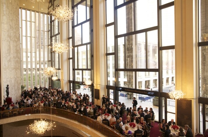 Guests dining at white-tablecloth tables in the Grand Tier lobby beneath glittering chandeliers and floor-to-ceiling windows.