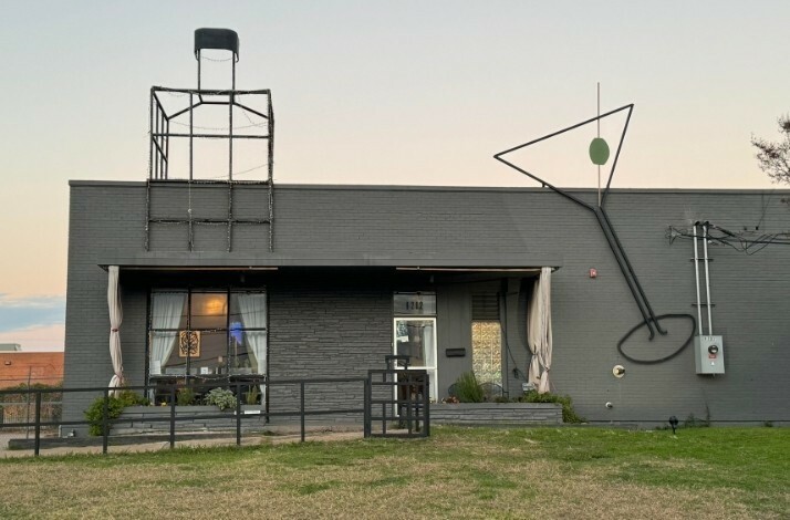 The building of New Artisan Distillery with a bottle and a cocktail glass made of tubes on the roof.