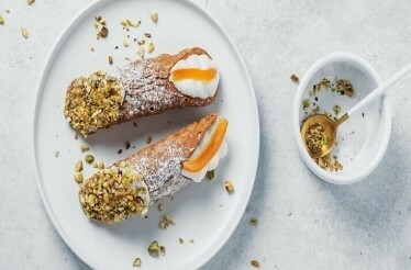 Two Sicilian cannoli topped with pistachios on a white plate.