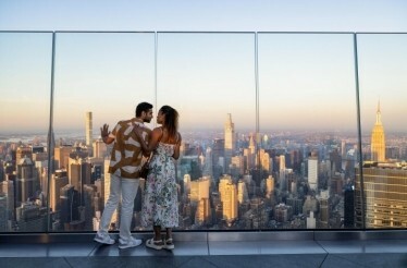 The couple are standing at the terrace by the panoramic view of the city.