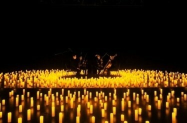 Musicians playing on stage, surrounded by thousands of flickering candles