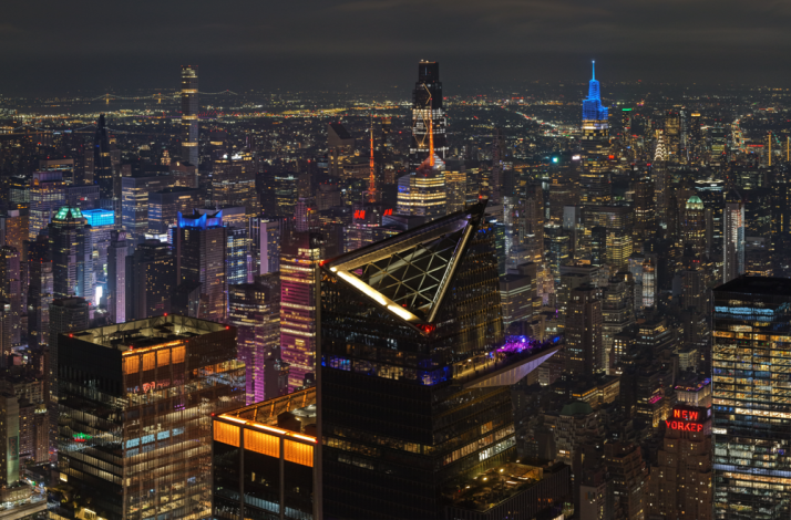 NYC skyline at night with Marquee Sky Deck lit up, city lights and iconic buildings visible.