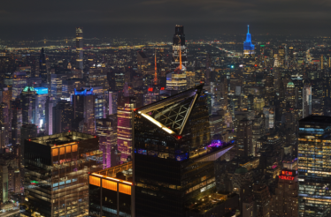 NYC skyline at night with Marquee Sky Deck lit up, city lights and iconic buildings visible.