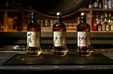 Three bottles of Nikka Japanese whiskey and tasting glasses lined up on a branded Quin Bar placemat.