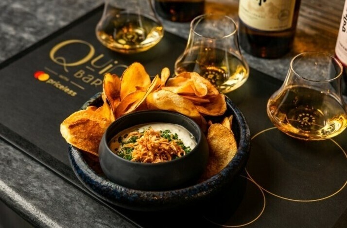 Whiskey flight glasses paired with a bowl of creamy dip topped with crispy onions and served with potato chips.