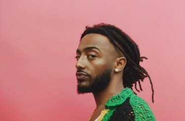 Promotional photo of music artist Aminé on a pink background.