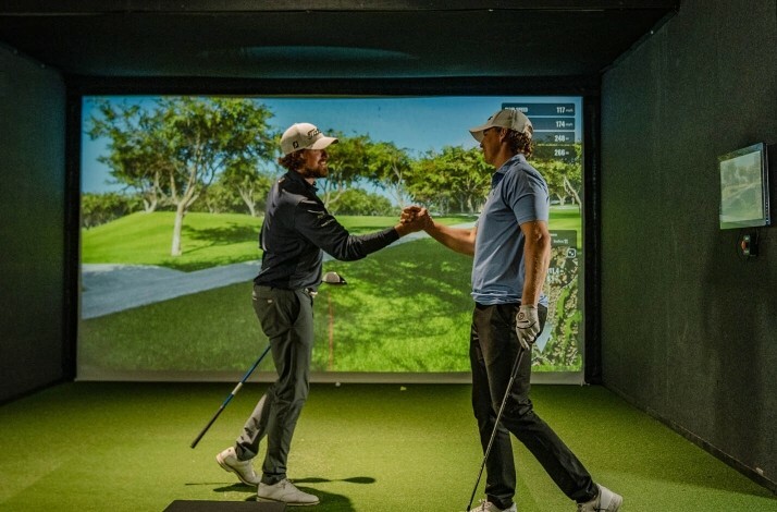 Two golfers shaking hands in an indoor golf simulator.