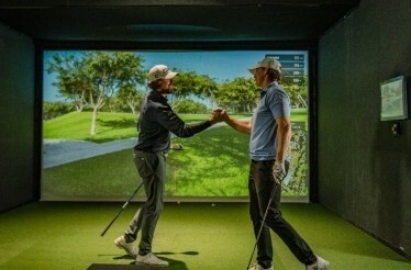 Two golfers shaking hands in an indoor golf simulator.