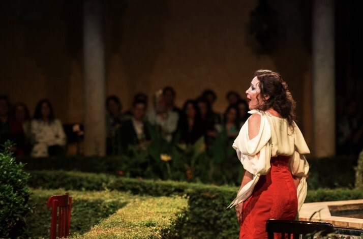Female Carmen opera performer in red skirt and white blouse performing with back turned, audience watching at Palacio de Las Dueñas.