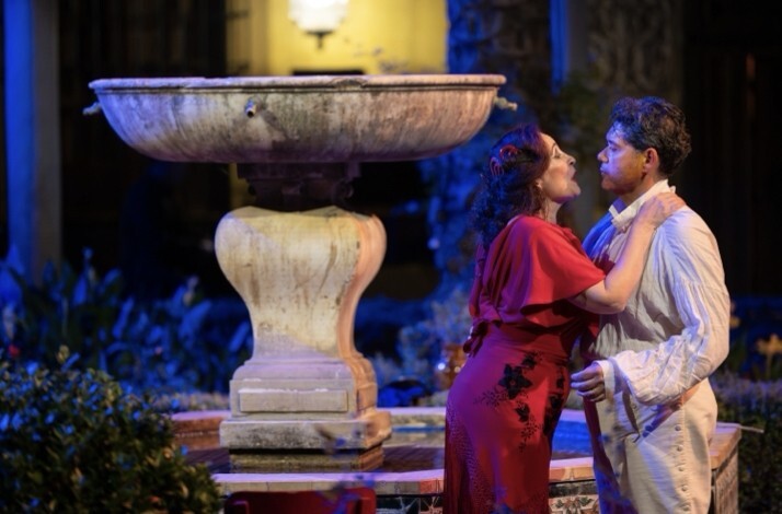 Two Carmen opera performers in an intimate embrace beside a stone fountain at night, Palacio de Las Dueñas, Seville.