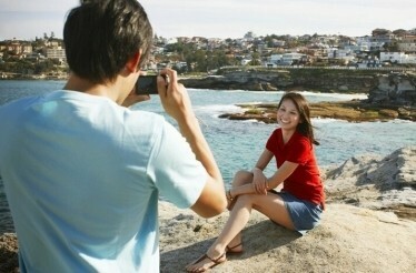 A man captures a photograph of a woman at the Bondi beach.