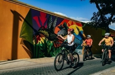 Three cyclists pass by the amazing street art at Oranjestad, Aruba.