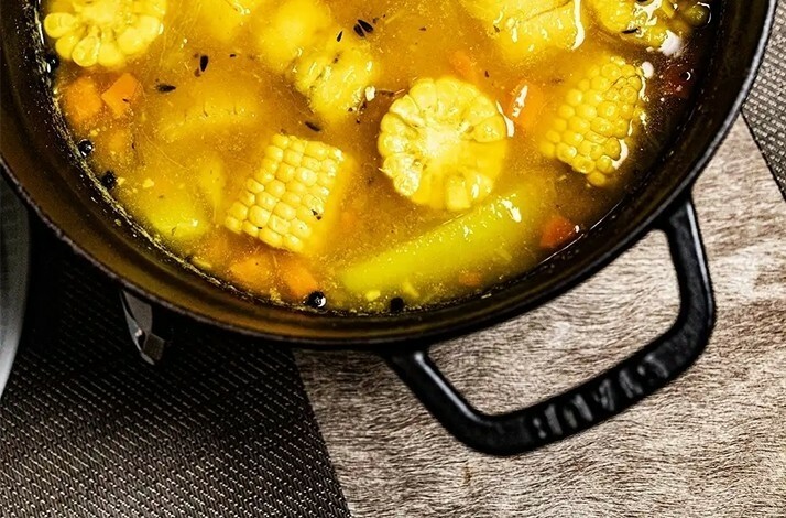 Vibrant corn soup in a black pot, bursting with rich flavors and spices