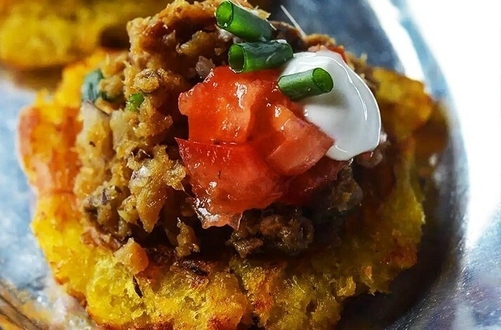 Savory plantain topped with seasoned meat, tomato, sour cream, and chives