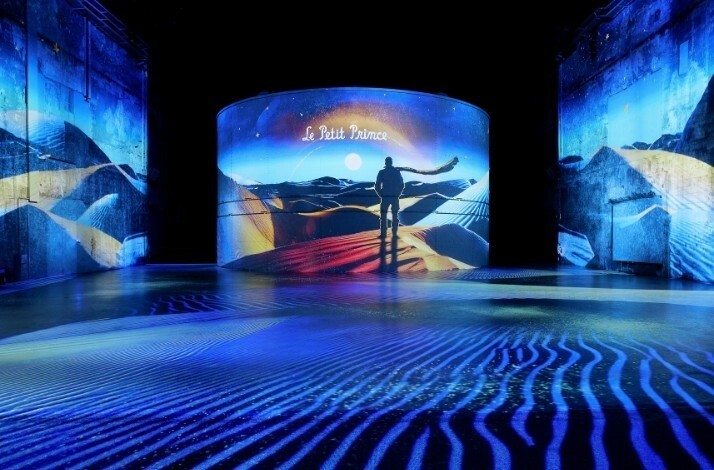 A digital projection of “Le Petit Prince” with a silhouette of the character standing in a vibrant desert scene.