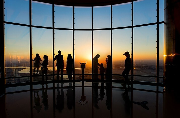 Visitors enjoying the sunset view of the city through panoramic windows At the Top, Burj Khalifa.