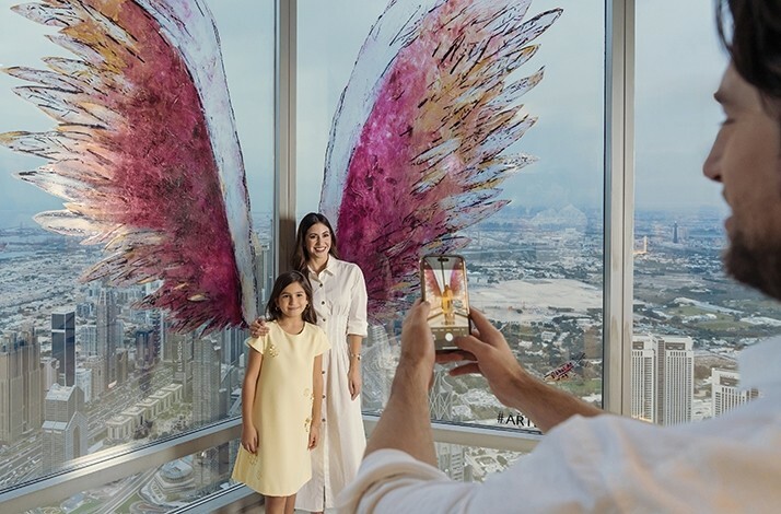 Happy family take a photo At the Top, Burj Khalifa with colorful wings on the panoramic window.