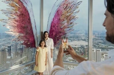 Happy family take a photo At the Top, Burj Khalifa with colorful wings on the panoramic window.