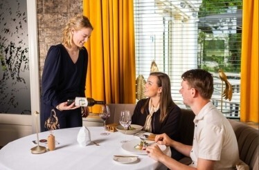 Sommelier pouring wine for a couple enjoying a five-course dinner at Hotel Carelshaven's elegant restaurant.