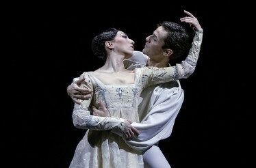 Two performers in period costumes dancing an intimate duet on stage.