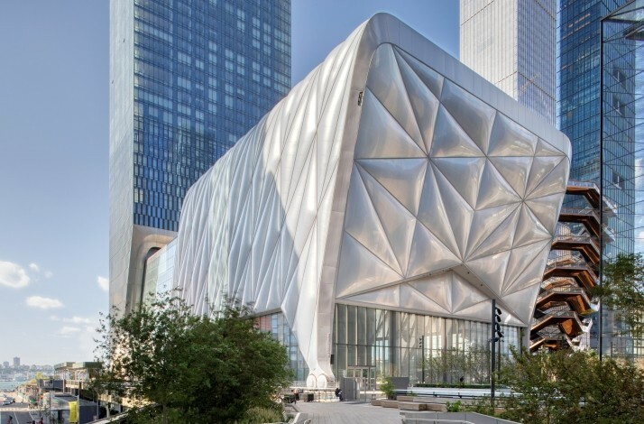 An exterior view of The Shed building, featuring a complex, alongside other high-rise structures in the cityscape