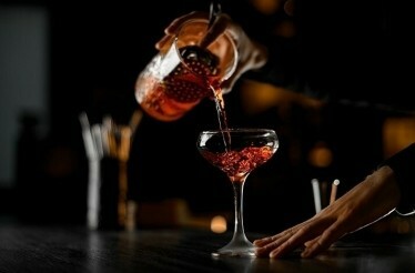 A bartender pours a cocktail from one glass into another at La Factoria.