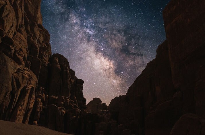  The Milky Way stretches across the night sky above a vast canyon, illuminated by countless stars.