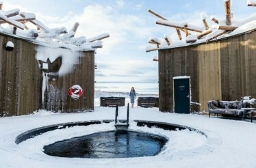 A person stands before a hot tub surrounded by snow at Ecolyx Arctic Bath winter spa