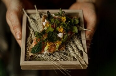 A dish served in a wooden plate and a pillow of ears of corn from a forest-to-plate menu at Michelin Green Star Restaurant Jord.