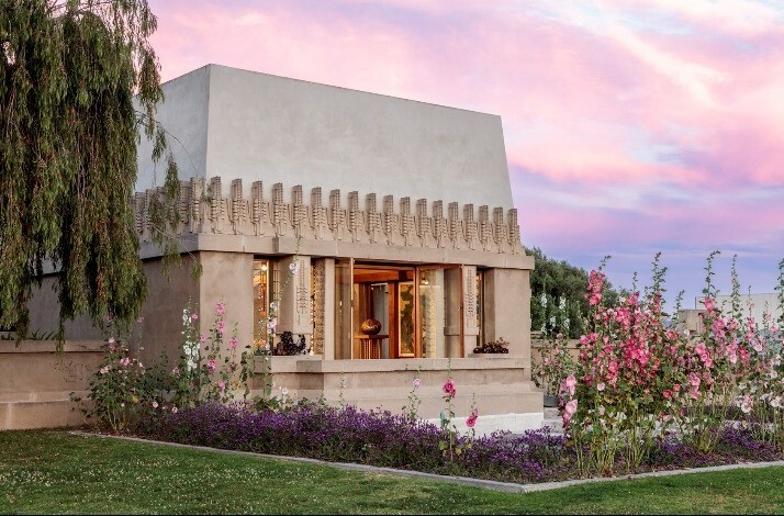 Outdoor exterior of Frank Lloyd Wright's Hollyhock House, surrounded with greenery and flowers.