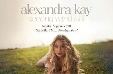 Promotional banner for Alexandra Kay, displaying the artist lying on a field, with flowers in her hair.