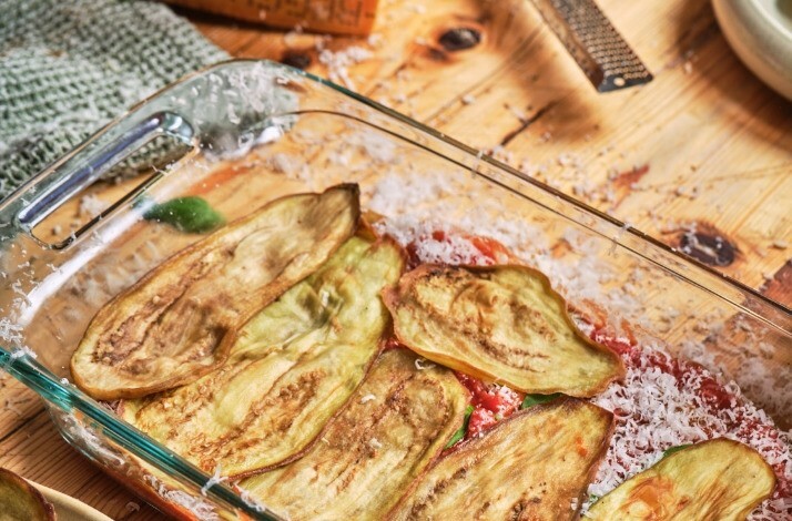 A glass dish filled with neatly arranged slices of eggplant, showcasing its rich purple color and smooth texture.