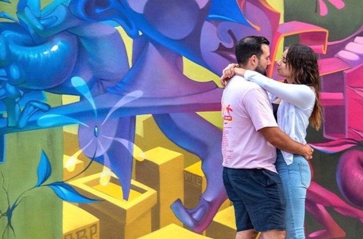 A couple poses in front of a wall art at the museum Wynwood Walls.