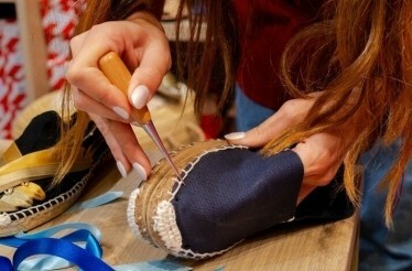 A woman is using scissors to cut a pair of shoes on a table.