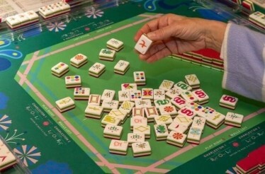 A player picking a Mahjong tile from a vibrant game board setup.