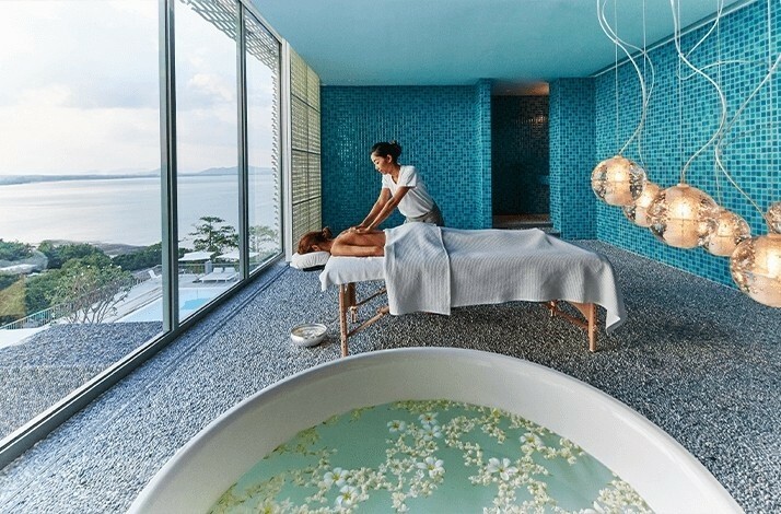 A person receiving a massage in a serene room with a panoramic view of the ocean.
