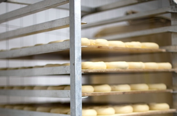 Rows of uncooked bagels proofing on a commercial sheet rack in the Russ & Daughters kitchen, NYC.