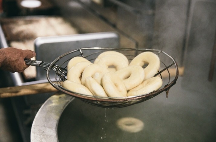 Baker's hand lifting freshly boiled bagels from a water bath using a wire skimmer at Russ & Daughters kitchen.