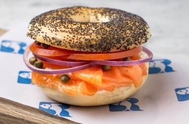 Poppy seed bagel layered with smoked salmon, cream cheese, tomato, red onion, and capers on Russ & Daughters paper.