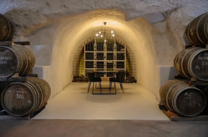 A stone-carved wine cellar at Hatzidakis Winery in Santorini, featuring rows of oak barrels and a cozy tasting area