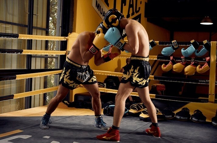 Two Muay Thai fighters spar in the ring with full protective gear.