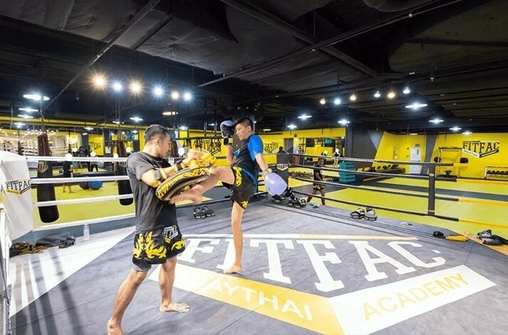 Two athletes train with focus mitts inside a Muay Thai ring.