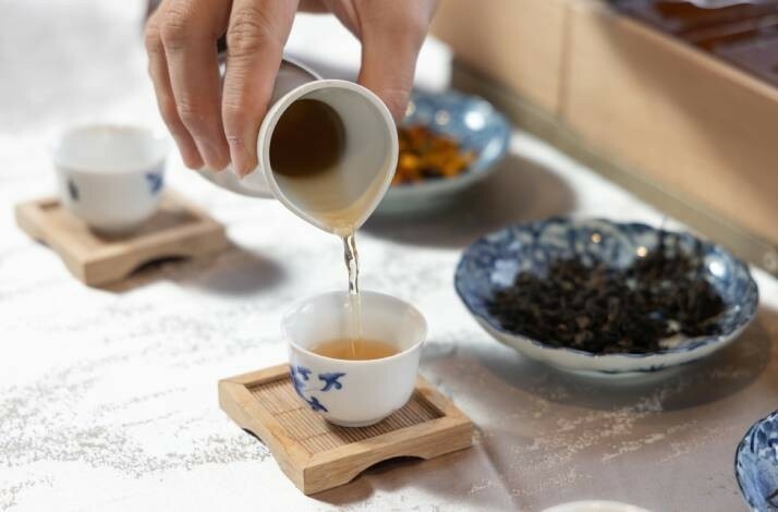 Tea is being poured into a small porcelain cup on a bamboo tray.