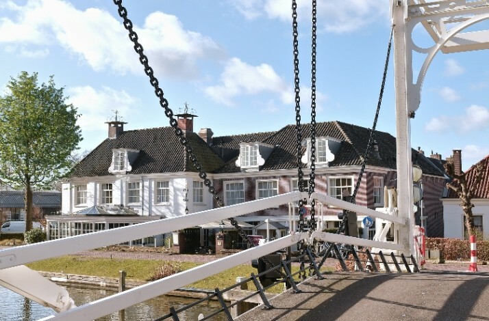 A charming view of a traditional Dutch drawbridge leading to the historic Hotel de Nederlanden by the canal, set under a clear blue sky