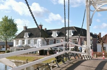 A charming view of a traditional Dutch drawbridge leading to the historic Hotel de Nederlanden by the canal, set under a clear blue sky